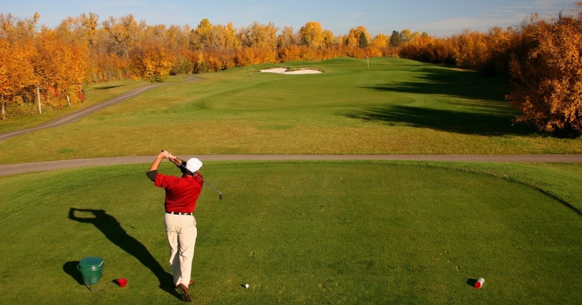 A golfer swinging on a sandy golf course. The image is in black and white.