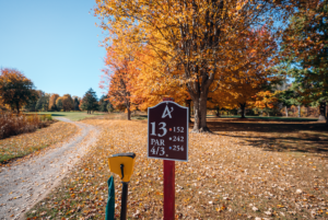 Hole 13 sign at Foothills Golf Course surrounded by autumn leaves and trees.
