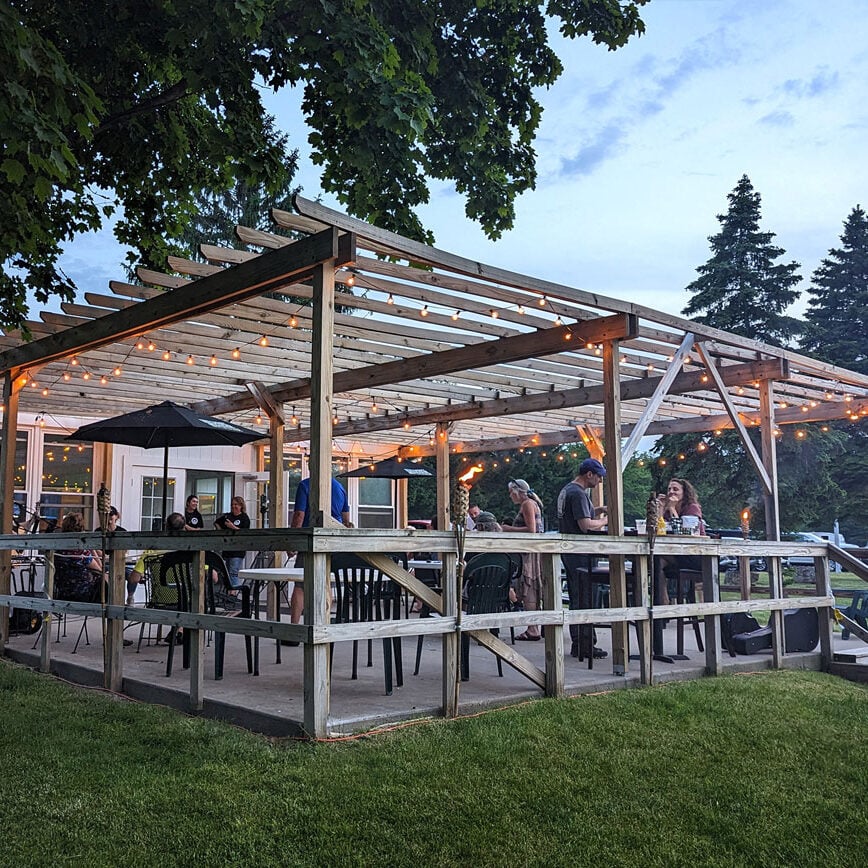 People dining on a patio with string lights. The patio is surrounded by trees.